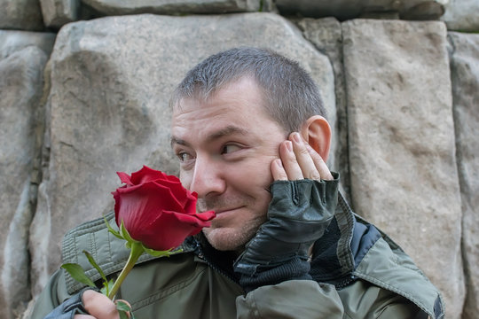 a guy on the street in an autumn jacket and leather gloves looks coquettishly and sniffs a red rose flower