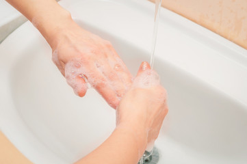 Young woman hands in soap. Washing hands, fingers in the sink. Soft room lighting.