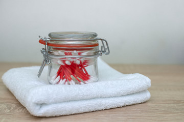 on a folded white towel is a glass jar with red cotton buds in the ear