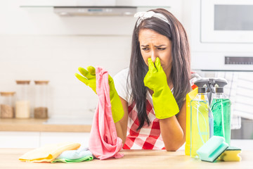 Female holding her nose with fingers upon smelly rag held in the other hand, leaning on kitchen...