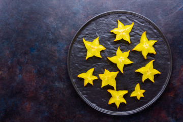 Carambola on a black plate. Sliced fresh carambola on a dark background. Slices of star fruit....