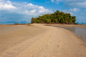 The sand spit to the island opened at low tide. Green trees on the island. Footprints of people on the sand. Beautiful clouds on the blue sky. Horizontal.