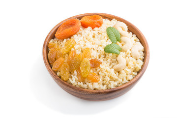 Bulgur porridge with dried apricots,  raisins and cashew in wooden bowl isolated on white background. Side view, close up.