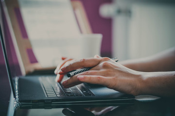 Die Frau arbeitet zu Hause, auf dem Tisch steht ein Computer und die Frau schreibt auf dem Computer