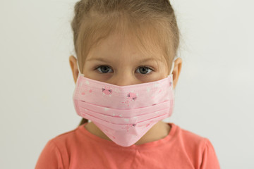 Portrait of caucasian little girl of four years old with surgical mask on face looking at camera indoor