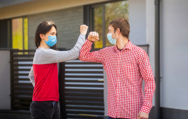 Elbows bump. Friends in protective medical mask on his face greet their elbows in quarantine. Elbow bump. Coronavirus, illness, quarantine, medical mask, COVID-19. Couple greeting with elbows