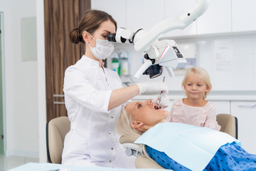 A dentist examines the oral cavity of her patient on the dentist's chair with the help of a special medical appliance