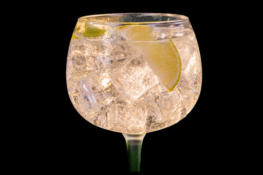 Alcohol drink (gin tonic cocktail) with lemon and ice on black background. Iced cocktail drink with lemon and herbs.