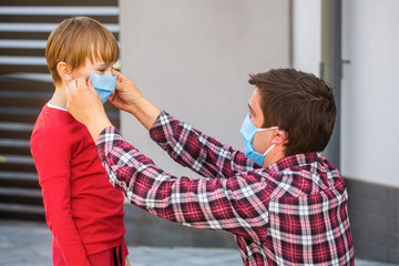 Father puts a medical mask on her son. Coronavirus, illness, infection, quarantine, medical mask, COVID-19. Father, child wear facemask during coronavirus, flu outbreak. Dad a son in a medical mask.