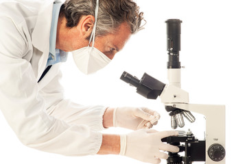 Scientific researcher with mask analyzing under a microscope