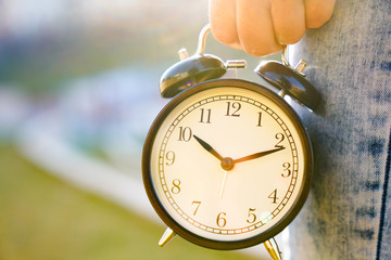 black alarm clock in a woman's hand on the background of nature. timeless and time concept image...