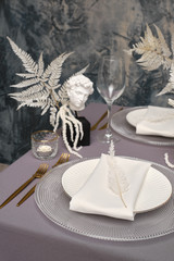 Luxurious stylish decoration of the wedding table for the winter wedding. Fresh and dried white flowers. Beautiful table setting: golden appliances, fork and knife, feather, wedding cake.