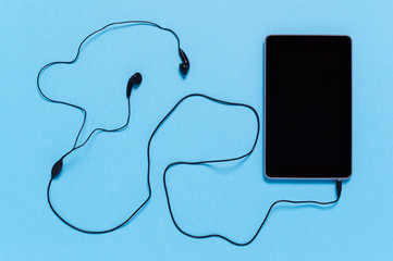 Black tablet with earphones on blue background. Minimal concept of connectivity, remote digital work or multimedia entertainment like music streaming
