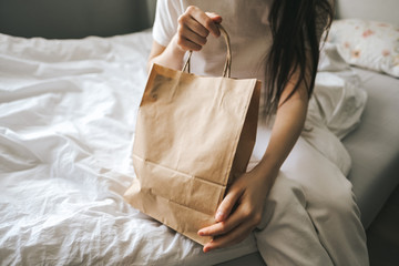 Woman holds craft eco shopping bag in  hands, sitting at home on sofa. Delivery food