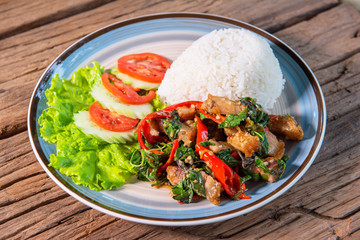 Crispy pork basil with rice, served with lettuce, cucumber, tomato, arrange a beautiful dish, put on a wooden table.