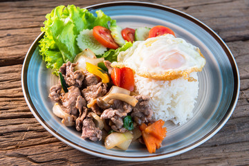 Stir fried beef with mushrooms, green peppers and onions topped with rice, fried eggs, Serve with lettuce, cucumber, tomato, arrange a beautiful dish, put on a wooden table.