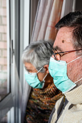 senior couple, with protective face masks, at home looking through the window. Concept of coronavirus quarantine stay home and social distancing. Lockdown people. elderly and retired lifestyle .