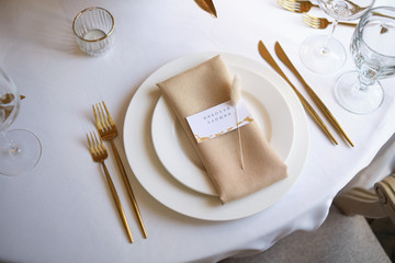Luxury cozy autumn wedding table decoration in the restaurant. Fresh and dried flowers, roses, carnations. Beautiful table setting: golden appliances, fork and knife, calligraphy guest seating card.