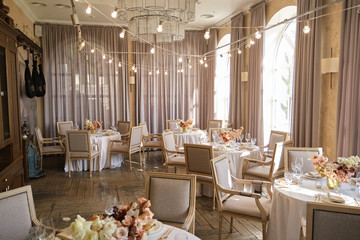 Luxury cozy autumn wedding table decoration in the restaurant. Fresh and dried flowers, roses, carnations. Beautiful table setting: golden appliances, fork and knife, calligraphy guest seating card.