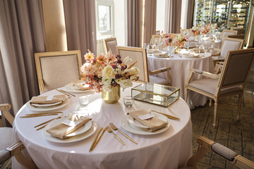 Luxury cozy autumn wedding table decoration in the restaurant. Fresh and dried flowers, roses, carnations. Beautiful table setting: golden appliances, fork and knife, calligraphy guest seating card.