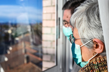 senior couple, with protective face masks, at home looking through the window. Concept of coronavirus quarantine stay home and social distancing. Lockdown people. elderly and retired lifestyle .