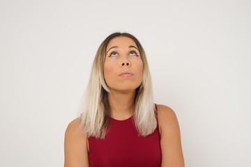 portrait of mysterious charming female with straight hair looking up with enigmatic smile. Beautiful smiling girl looking up standing against gray wall.