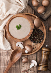 Fototapeta na wymiar Wooden plate of creamy chestnut champignon mushroom soup with wooden spoon, pepper and kitchen cloth on wooden background.