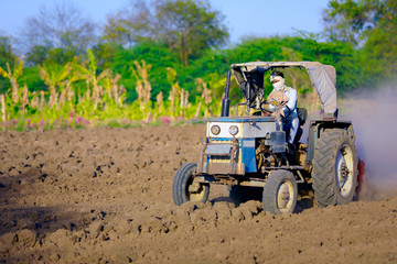 Indian / Asian farmer with tractor preparing land for sowing with cultivator, An Indian farming...