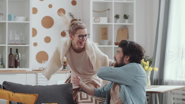 Joyous woman snatching smartphone off hands of husband while he surfing the Internet. Cheerful man pulling laughing wife on couch and taking off phone