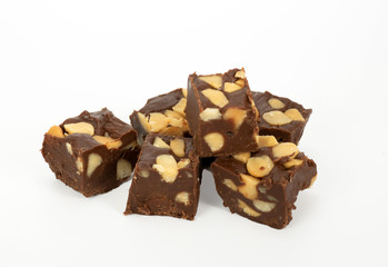 Chunks of homemade chocolate macadamia nut fudge stacked against a white background.