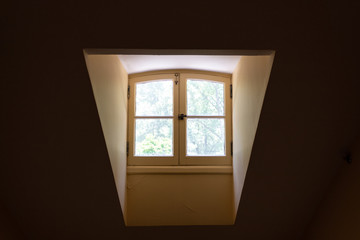 Narrow dormer window as seen from the inside of a darkened room with sunlight streaming in,...