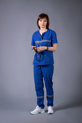 Portrait of a young nurse holding a stethoscope. Posing on a gray background. Girl in medical clothes.