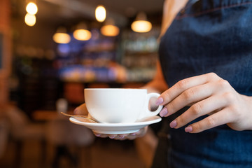 Hand of young waitress with cup of tea or coffee carrying it to one of clients