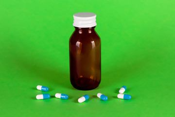 Big medicine glass bottle with blue capsules, cap on and green background