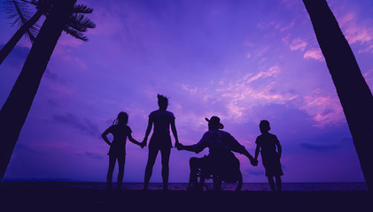 Disabled man in a wheelchair with his family on the beach. Silhouettes at sunset