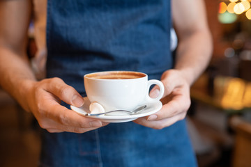 Hands of young waiter of classy restaurant carrying cup of fresh cappuccino