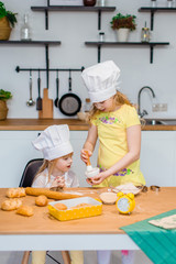 Family scene at white kitchen - two nice little sisters baking cookies and buns