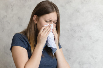 Sick woman with handkerchief sitting at home with flue, virus, cold, seasonal allergy symptom. Young woman blows her nose or sneezing in a blue cloth handkerchief