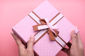 women hand holding pink color gift box on pink background.