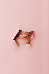 Girl female lips Hole In Pink Paper.Woman looking in the hole, bright beautiful makeup, big eyes and lips, bright lipstick, professional cosmetics and facial care.
