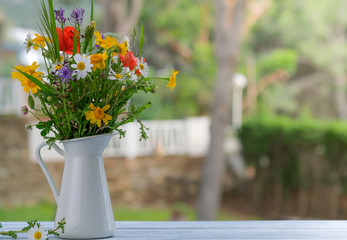 Still life with bouquet of spring wildflowers against green natural backdrop. Wild flower bouquet in white jug on vintage wooden table. Beautiful floral background with copy space.