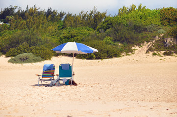Two chairs and an umbrella on a beach with a green nature in the background.