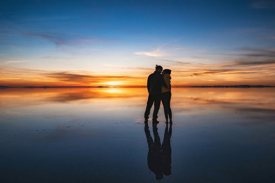 Young couple kissing and watching sunrise at Uyuni Salt Flats (Spanish: Salar de Uyuni ) in Bolivia, South America, romantic holiday and honeymoon travel concept. 