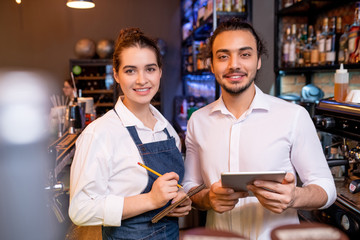 Two young cheerful workers of classy restaurant or cafeteria meeting guests