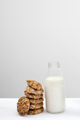 An open bottle of milk with oatmeal cookies sprinkled with sesame seeds and almonds on a table against a gray wall in the kitchen