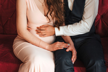 The man and woman are expecting a baby, the husband supports his wife's stomach, they hold hands and full of Love
