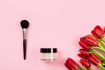 Obraz na płótnie Canvas Tools for applying light refreshing makeup lie on a pink background with a bouquet of red tulips. Bright spring-summer collection. Trendy background for advertising text.