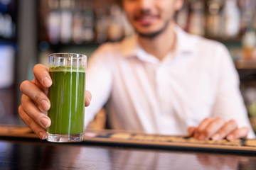 Hand of waiter putting glass of vegetable smoothie of green color on bar counter