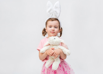 A cute girl on a white background with an empty seat. A girl with hare ears and a stuffed rabbit toy. A little girl in a pink t-shirt. The girl looks at the camera