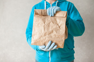 Contactless delivery of goods. The food delivery courier is holding a large paper bag in his hands. Man in rubber gloves and a medical mask.